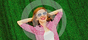 Portrait of happy smiling young relaxing woman lying on the grass background in park