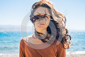 Portrait of happy smiling young woman on beach and sea background. Wind plays with girl long hair