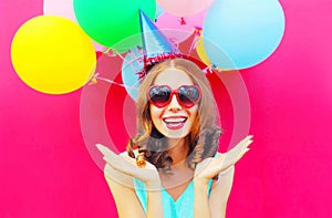 Portrait happy smiling young woman in a birthday cap is having fun over an air colorful balloons pink