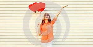 Portrait of happy smiling young woman with bunch of red heart shaped balloons wearing shirt, sunglasses on white background