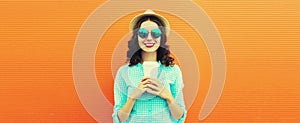 Portrait of happy smiling young woman with coffee cup wearing summer straw hat on orange background, blank copy space for