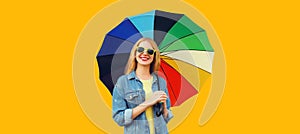 Portrait of happy smiling young woman with colorful umbrella isolated on yellow background