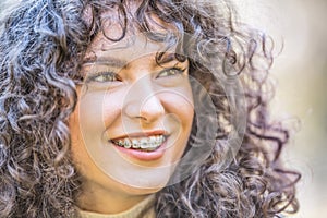 Portrait of a happy smiling young woman with dental braces and and curly hair