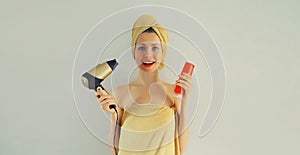 Portrait of happy smiling young woman drying wet hair in wrapped bath towel and holding bottle of shampoo after taking a shower