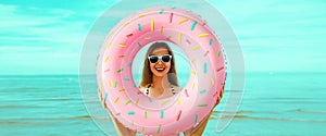 Portrait of happy smiling young woman with inflatable ring wearing straw hat on beach on sea background