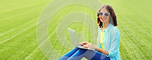 Portrait of happy smiling young woman with laptop in summer park on green grass background