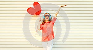 Portrait of happy smiling young woman listening to music in headphones holding bunch of red heart shaped balloons on white