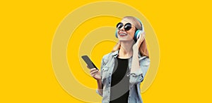 Portrait of happy smiling young woman listening to music in wireless headphones with smartphone isolated on vivid yellow