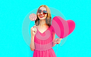 Portrait happy smiling young woman with lollipop, pink heart shaped air balloons on colorful blue