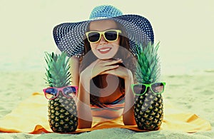 Portrait happy smiling young woman lying on a beach with funny pineapple wearing a straw hat