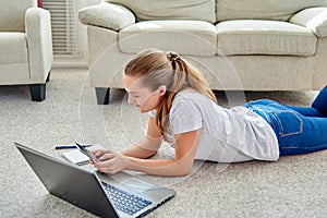Portrait of happy smiling young woman lying on floor with laptop and using smartphone at home, copy space