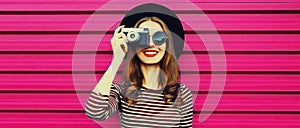 Portrait of happy smiling young woman photographer with vintage film camera on colorful pink background