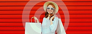 Portrait of happy smiling young woman with shopping bags wearing straw hat and shirt on colorful red background