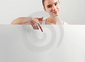 Portrait of happy smiling young woman, showing empty blank signboard with copyspace.