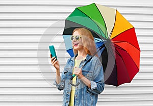 Portrait happy smiling young woman with smartphone and colorful umbrella on a white background