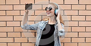 Portrait of happy smiling young woman taking selfie picture by smartphone in wireless headphones listening to music
