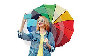 Portrait of happy smiling young woman taking selfie by smartphone with colorful umbrella isolated on white background
