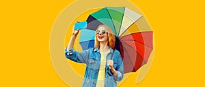Portrait of happy smiling young woman taking selfie by smartphone with colorful umbrella isolated on yellow background