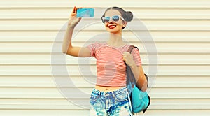 Portrait happy smiling young woman taking a selfie by smartphone wearing backpack on white background