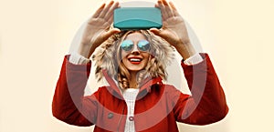 Portrait of happy smiling young woman taking selfie with smartphone wearing red jacket with fur hood