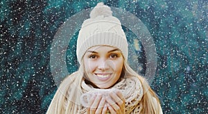 Portrait of happy smiling young woman wearing knitted hat and scarf in winter over a snowflakes background