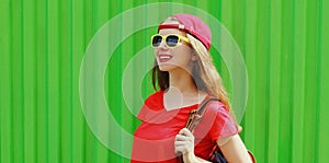 Portrait happy smiling young woman wearing a red baseball cap and backpack in a city