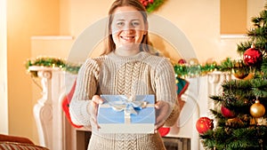 Portrait of happy smiling young woman in wool sweater holding Christmas gift in box and showing it in camera. Perfect