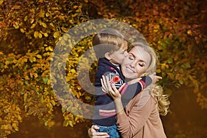 Portrait happy son strong kiss his mother in a park in the autumn