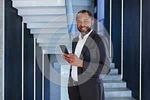Portrait of happy successful African American boss, man smiling and looking at camera, businessman holding phone using