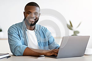 Portrait Of Happy Successful Black Freelancer Guy Posing At Desk With Laptop