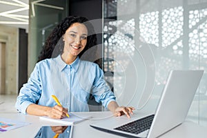Portrait of happy and successful hispanic woman, businesswoman smiling and looking at camera holding contracts and