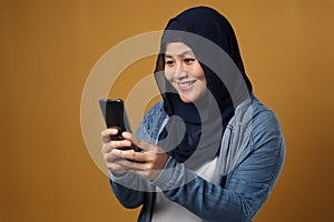 Portrait of happy successful muslim Asian woman smiling while reading message text good news on her smart phone, over yellow