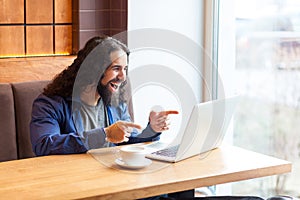 Portrait of happy suprised handsome young adult man freelancer in casual style sitting in cafe and watching funny video in laptop