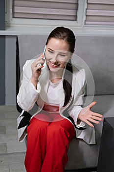 portrait of happy, surprised, excited brunette business woman talking by phone in gray office. gain, good phone call