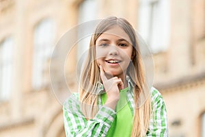 Portrait of happy teen girl smiling with finger on cheek blurry outdoors
