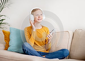 Portrait of happy teen girl wearing wireless headphones listening music on smartphone