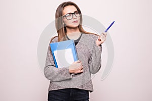 Portrait of a happy teenage girl with backpack holding books while standing and pointing finger up at copy space isolated over whi