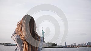 Portrait of happy tourist woman with flying hair enjoying New York skyline at Statue of Liberty from a boat slow motion.