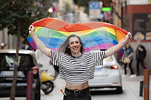 Portrait of a happy transgender girl waving a rainbow flag in a city street. LGBTQ community and diversity concept