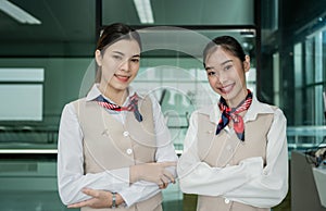Portrait of happy two Asian flight attendants in uniform standing and arms crossed with confidence in airport terminal