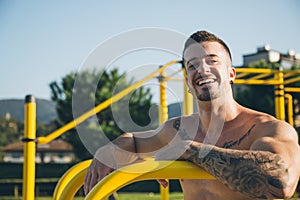 Portrait of a happy urban athlete with tattoos at the calisthenics gym