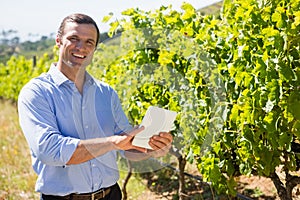 Portrait of happy vintner using digital tablet in vineyard