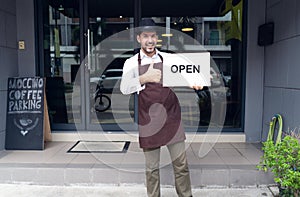 Portrait of a happy waitress standing at coffee shop entrance and holding open sign in front coffee shop. Startup Small Business