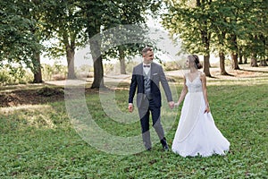 Portrait of happy wedding couple walking on green grass in park in summer. Young attractive woman looking at young man.