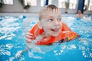 White Caucasian child in swimming pool. Preschool boy training to float with red circle ring in water