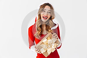 Portrait of happy woman 20s wearing Santa Claus red costume smiling and holding present box, isolated over white background