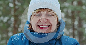 Portrait of a happy woman 60s blowing snow from her hands towards the camera