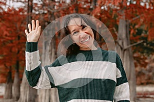 Portrait of happy woman in autumnal park. Stylish woman greets and say hello