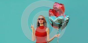 Portrait happy woman with bunch of red heart shaped balloons blowing her lips on a blue background