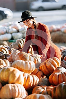 Portrait of happy woman choosing ripe orange pumpkin on farmers market in brown sweater, dress. Cozy autumn vibes Halloween,